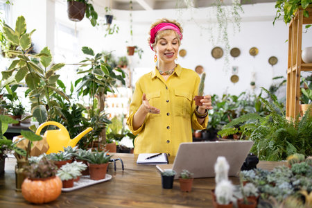 A woman in a yellow shirt is holding a cactus while teaching about plants in a bright, green environmentの写真素材