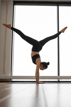 A woman in black athletic wear executes a challenging yoga pose, balancing on her hands with legs...