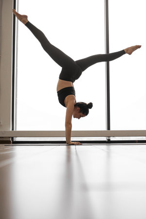 A woman in athletic wear balances on her hands with her legs extended in a split, performing a...