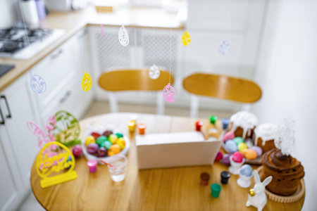 A kitchen table is set up for Easter baking and decorating with colorful eggs, cakes, paints, and festive ornamentsの写真素材