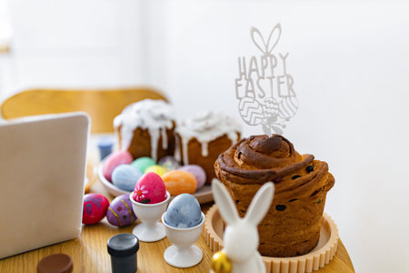 A festive table setting features traditional Easter cakes, colorful painted eggs in holders, and a Happy Easter cake topper with bunny earsの写真素材