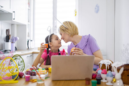 A mother and daughter share a tender moment while decorating Easter eggs together in a bright kitchenの写真素材