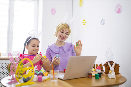 A mother and daughter enjoy decorating Easter eggs together while participating in an online class, fostering family bonding and festive creativityの写真素材