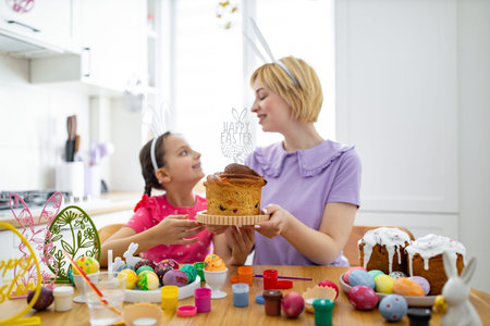 A mother and daughter wearing bunny ears are preparing for Easter, surrounded by painted eggs and...