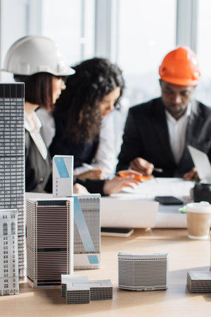A diverse team of architects collaborates around a table, reviewing blueprints and miniature building models, symbolizing urban planning and design