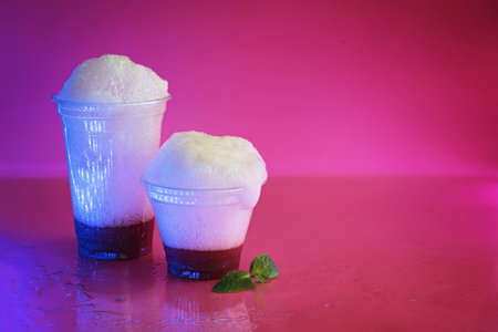 Oxygen cocktail foam in the two plastic glasses on a bright pink background with a sprig of mintの写真素材
