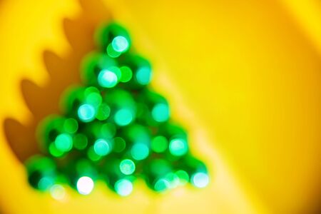 Abstract christmas new year bokeh lights in shape of green christmas tree on yellow backgroundの写真素材