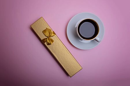 Cup of espresso coffee and golden gift box on a pale pink background. Flatlay. View from above.の写真素材