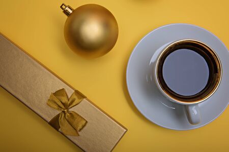 Cup of espresso coffee, golden gift box and golden Christmas ball on a yellow background. Flatlay. View from above.の写真素材