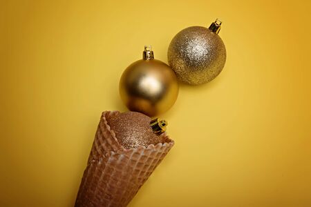 Golden christmas balls in ice cream waffle cone on yellow background.の写真素材