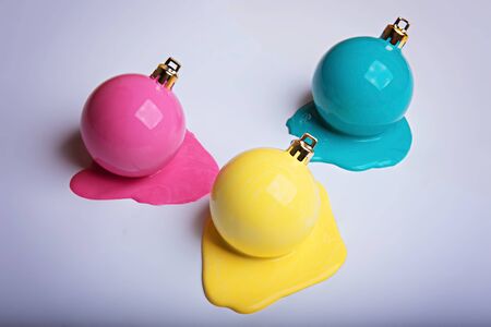 Three New Years Christmas balls painted in pale pink, yellow and turquoise lay in a puddles of paint on a white sheet of paper.の写真素材