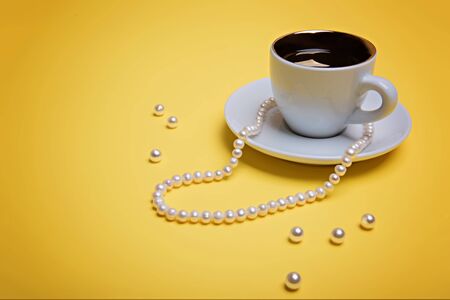 A cup of espresso, pearl beads and a few beads are on a yellow background.の写真素材