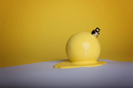 New Years Christmas ball painted in yellow lay in a puddle of paint on a white sheet of paper. yellow background. Monochrome.の写真素材