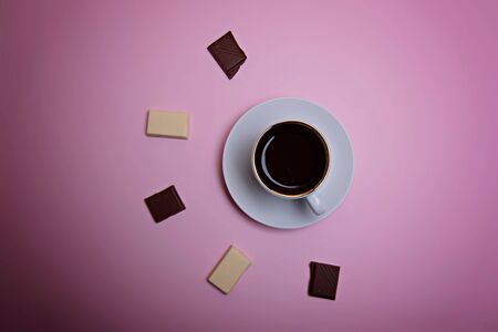 A cup of espresso coffee, pieces and crumbs of dark and white chocolate on a pale pink background. Flatlay. View from above.の写真素材