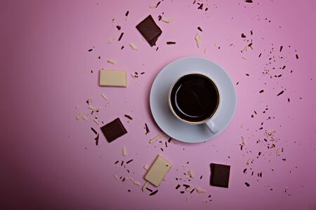 A cup of espresso coffee, pieces and crumbs of dark and white chocolate on a pink background. Flatlay. View from above.の写真素材