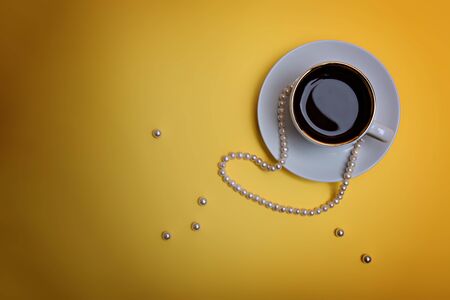 A cup of espresso, pearl beads and a few beads are on a yellow background. Flatlayの写真素材