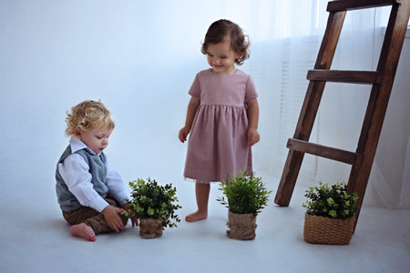 Little boy and girl are playing with plants near the wooden stairs in a bright room.