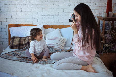 Happy loving family. Mother playing with her daughter child girl on the bed and and photographing her.の写真素材