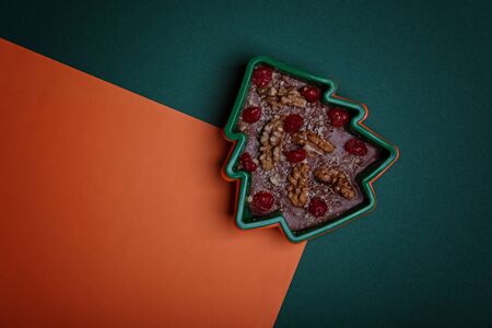 Handmade chocolate in the shape of a Christmas tree with cranberries and nuts on a green and orange background.の写真素材