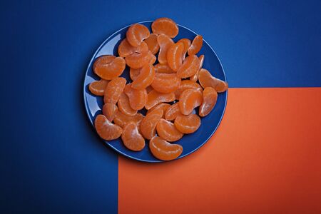 Many peeled mandarin slices on the blue plate. Classic blue background. Color of the year 2020, Classic Blue.の写真素材