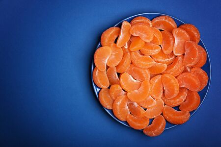 Many peeled mandarin slices on the blue plate. Classic blue background. Color of the year 2020, Classic Blue.の写真素材
