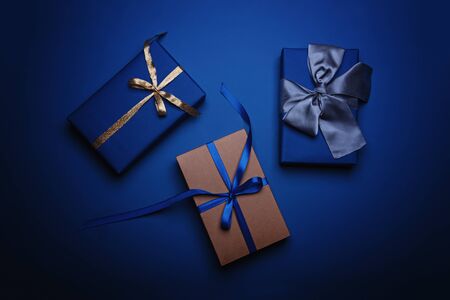 Three gift boxes wrapped in classic blue paper with a gold, blue and grey ribbons. Color of the year 2020, Classic Blue. Copy space.の写真素材