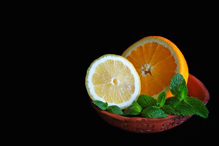 Citruses lemon and orange with mint in a ceramic bowl on the black backgrondの写真素材