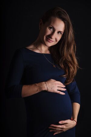 Portrait of the pregnant woman hugs her belly with love on the black background.の写真素材