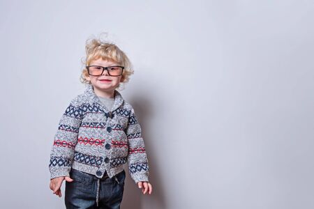 A little boy with blond curly hair looks in glasses smiles. On a white background. Copy space. Place for text.の写真素材