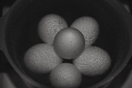 Chicken eggs are boiled in a pan. Black and white.