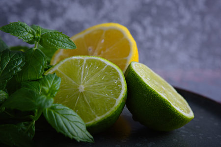 Lime, lemon and mint leaves lie on a plate on the gray background.