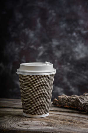 Paper cup of coffee and a piece of bark on a wooden table on a dark background. Natural materials.の写真素材