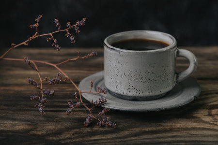 A cup of espresso coffee on a wooden table on a dark background. A sprig of dried flowers nearby.の写真素材