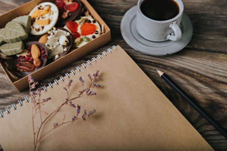 Chocolates with dried fruits in a box and craft paper notebook near the cup of coffee. Place for your text.の写真素材