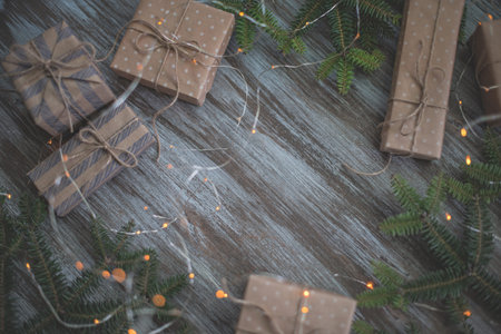 Christmas background. Gift boxes wrapped in craft paper, fir branches and garland lights.
