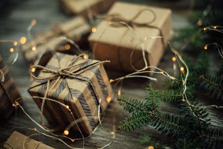 Christmas background. Gift boxes wrapped in craft paper, fir branches and garland lights.の写真素材