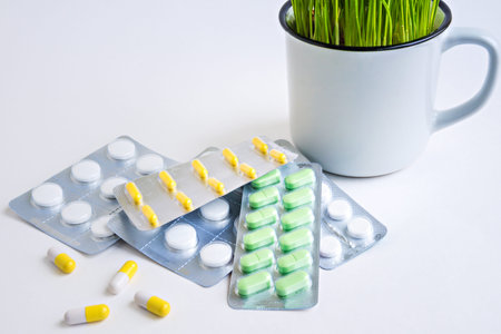 Green grass in the cup and blisters of pills on white background.
