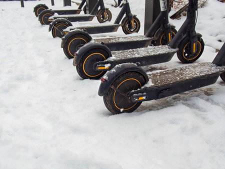 Electric urban transportation: the row of electric readies to ride scooter bikes with accumulators parked in the snow in winter.の写真素材