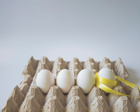 White eggs with yellow gift ribbon in an egg carton on a white background.