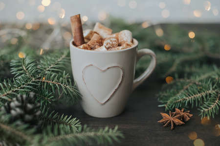 Winter Christmas beverage on the background of fir branches and garland lights on a wooden table.の写真素材
