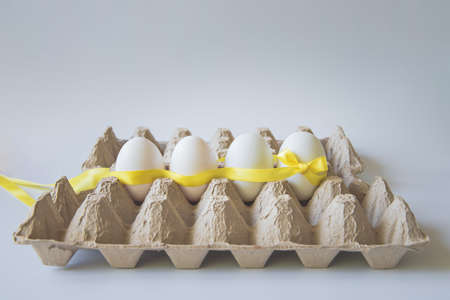 White eggs with yellow gift ribbon in an egg carton on a white background.の写真素材