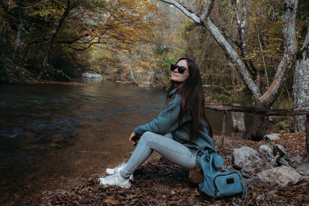Caucasian girl with long dark hair sits on the river bank. Hiking.の写真素材