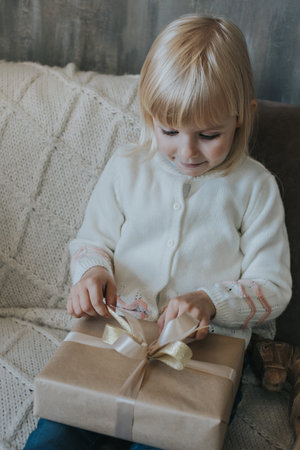 Little girl with blond hair opens a Christmas present.