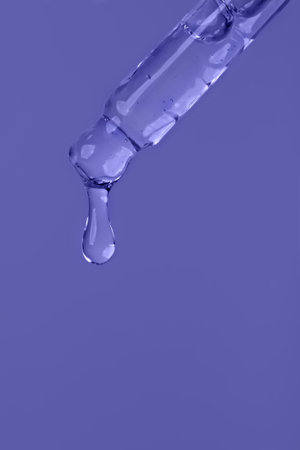 Cosmetic serum. Dropper with a drop and a bottle on a lavender purple background. Copy space. Place...