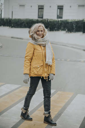 Aged pretty woman with blond hair crossing the road at a pedestrian crossing.の写真素材