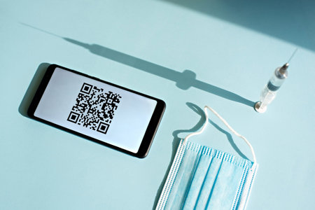 Smartphone with quar code of vaccination certificate on the screen, syringe and medical mask on a...