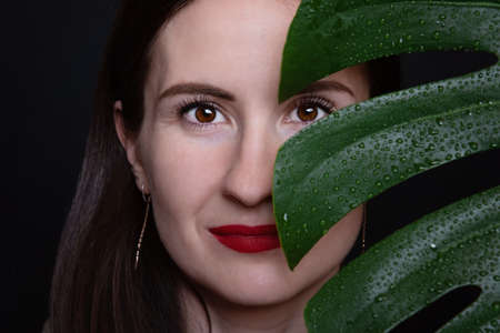 Female portrait. The girl looks through the monstera leaf.の写真素材