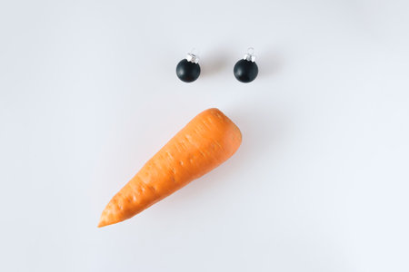 Creative snowman face made of carrots and black Christmas balls on a white background.の写真素材
