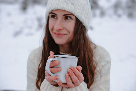 A woman in a white knitted sweater holds a white mug with a hot drink in her hands. Selective focus.の写真素材
