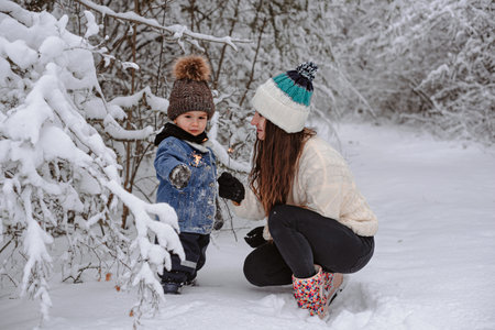 Mom and son are walking in the snow and light sparklers in the forest.の写真素材